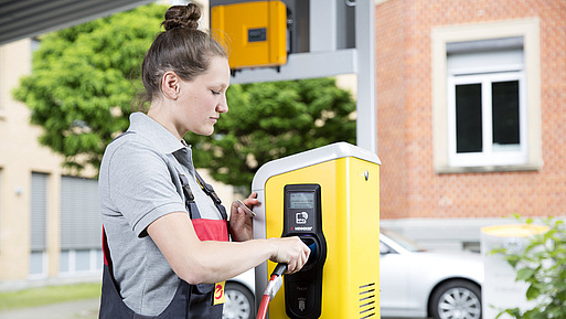 Elektrikerin steckt E-Auto-Stecker in Ladesäule